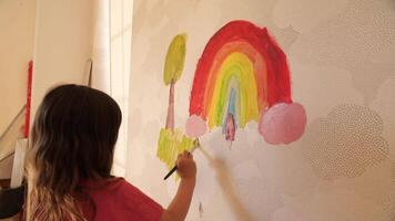 Little girl painting rainbow and tree on wall with brush video