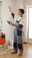 A man in overalls standing in front of a wall with a tablet video