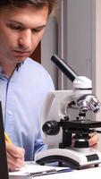 vertical Scientist using microscope and taking notes in laboratory video