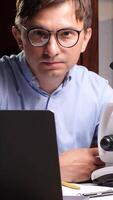 vertical Scientist working with laptop and microscope in laboratory doing research video