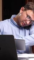 A man in glasses sitting at a desk with a laptop and papers video