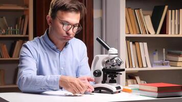 Close-up portrait scientist sitting at desk in his office or laboratory and counting coins, concerned about research funding next to a microscope and bookshelves video