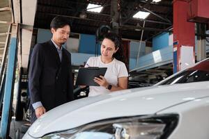 Warranty service business work, Latino female client inspections sign contract document from Asian male insurance agent, accept claims car fix from accident and maintain at automobile garage. photo