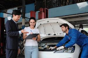 Warranty service work, Latin female client cheerful sign contract document from Asian male insurance agent, accept claim car fix from accident, mechanic behind at maintain automotive garage. photo