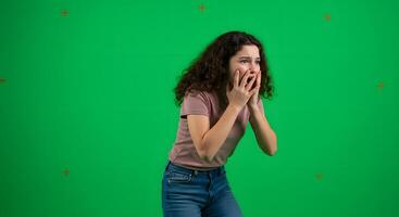 A woman is holding her hands to her face while standing in front of a green screen photo