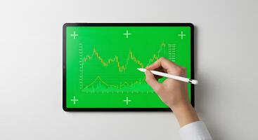 Hand holding a tablet with a green screen showing a graph photo