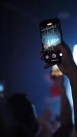 Spectators capturing moments at a live music concert, holding smartphones to record performances under vibrant blue and white stage lights, creating a lively atmosphere filled with excitement video