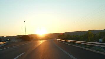 Golden sunlight bathing asphalt roadway, vehicle traveling scenic highway, capturing expansive landscape during warm evening light with sweeping horizon view video
