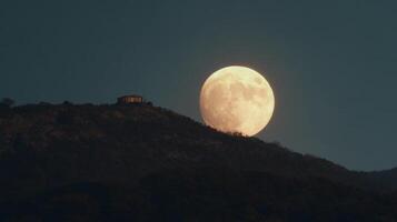Majestic Full Moon Rising Over Serene Mountain Landscape at Dusk with Silhouette of Structure on Hilltop photo