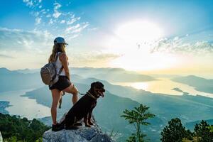 A sporty girl with a backpack stands on the edge of a mountain with a Rottweiler dogSporty girl with backpack on mountain edge photo