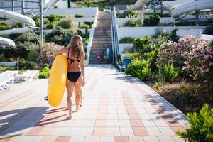 A slender girl walks through the water park and carries a yellow photo