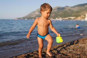 Little boy runs along the sandy shore with a toy sprinklerLittle boy runs on sandy shore with toy sprinkler photo