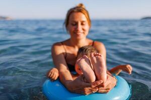 A young mother shows the legs and arms of her baby, who is sitting in an inflatable ring in the seaBaby in Inflatable Ring with Mother photo