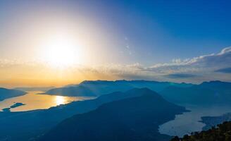 Dazzling sun in the evening sky illuminates all the peaks of the Balkan Montenegrin mountains and the coast of Kotor BaySunlight shines on Balkan Montenegrin mountains photo