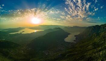 Panorama of dazzling sun in the evening sky illuminates all the peaks of the Balkan Montenegrin mountains and the coast of Kotor Bay photo