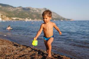 Little boy runs along the sandy shore with a toy sprinklerLittle boy runs along sandy shore with toy sprinkler photo