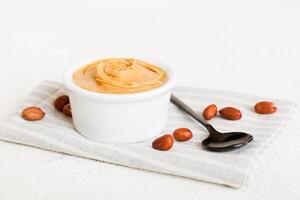 Bowl of peanut butter and peanuts on table background. Creamy peanut pasta photo