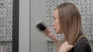 Woman brushes her long straight hair at home in front of a mirror video