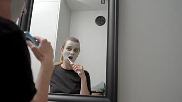 Woman with facial mask brushes her teeth in front of the bathroom mirror video