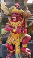Vivid close-up of colorful Hanuman statue guarding temple entrance in Bali, Indonesia. Hindu monkey deity with golden crown and mace stands in front of temple doors. video