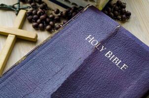 The Holy Bible and Holy Rosary placed beside wooden table photo