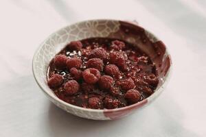 A photograph of a ceramic bowl filled with glistening raspberry jam photo