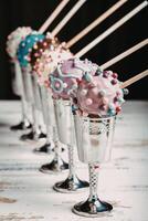 Colorful cake pops in the metal wineglasses on a wooden table photo