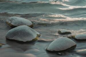 A photograph of weathered gray rocks jutting out from turbulent turquoise water. photo