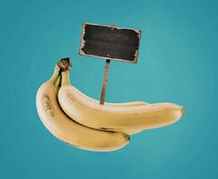 bunch of ripe yellow bananas and wooden signpost with empty black space, blue background photo