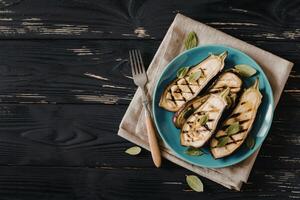 Grilled eggplants in plate has fork on isolated on black wood background photo