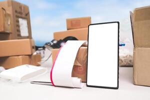 Smartphone with blank screen and receipt on table surrounded by cardboard boxes for online delivery. photo