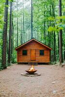 Cozy cabin surrounded by tall trees and a fire pit in the foreground. Summer break camp escape concept. photo