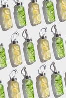 Top view glass bottles, water drink detox with lemon and cucumber at sunlight on white background, geometric pattern. Infused water with slices fruit or vegetable. Aesthetic photo with drinks