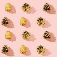 Christmas pattern from natural pine cone painted golden colored on pink. photo