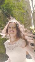 Smiling bride in a flowing dress runs toward the camera through rocks. The sun s backlight creates flashes and warmth, capturing energy and happiness. video