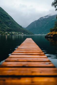 Wooden Dock Extending Over Calm Lake Surrounded by Mountains Under Cloudy Sky. photo