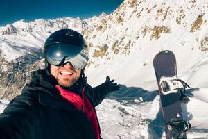 Happy excited snowboarder taking a selfie after reaching top before freeriding in caucasus mountains outdoors photo