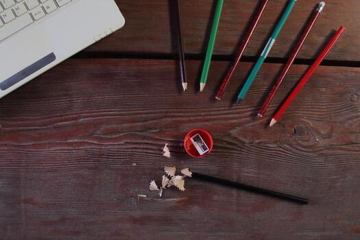 On the wooden table there is a red sharpener and pencil shavings. On the left is a laptop. The concept of learning photo
