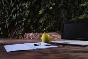 There is a laptop on the street table, and a notepad is open next to it. photo