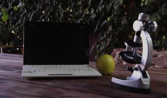 There is a microscope, a laptop, and a green apple on a wooden table. Concept of learning and research photo