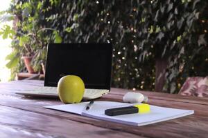 The laptop sits on a wooden table, with a notepad and a pen and bright green marker in the foreground. photo