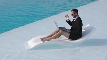 A freelancer works online on a laptop while lying on a sun lounger by the pool, enjoying summer. Concept remote work, freedom, relaxation and summer vibes video