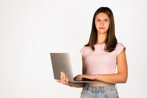 Teenage girl with straight brown hair wearing a pink t-shirt and denim shorts holds a laptop, isolated on white background. Suitable for technology, education, online learning, remote work, and youth lifestyle concepts. photo