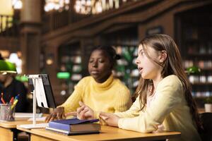 Diverse schoolgirls at a study table attending virtual webinar class, focusing on e learning and academic activity via internet connection. Students chatting with their teacher on live web seminar. photo