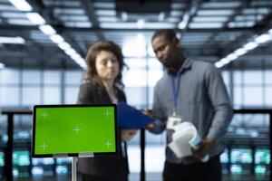 Green screen laptop used by system administrators in data center inspecting supercomputers, updating network topologies. Close up of mockup notebook next to man and woman in server farm photo