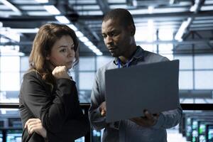 Computer scientists in data center using laptop to develop disaster recovery plans. IT professionals in server farm discussing, testing failover scenarios, protecting data during disruptions photo