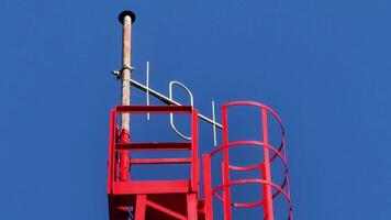 A striking red communication tower stands tall against the brilliant, clear blue sky above photo
