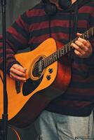 de cerca de persona jugando acústico guitarra, vistiendo a rayas capucha y auriculares. ver de manos y guitarra detalles, enfatizando el Actuar de jugando música. foto