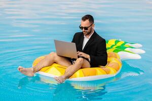 Young man sitting on an inflatable in a pool using a laptop. Concept remote work, freelance lifestyle. photo