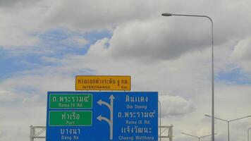 Close-up view of bright Thai expressway signs with bilingual directions under a partly cloudy sky, illustrating highway navigation in Bangkok. photo